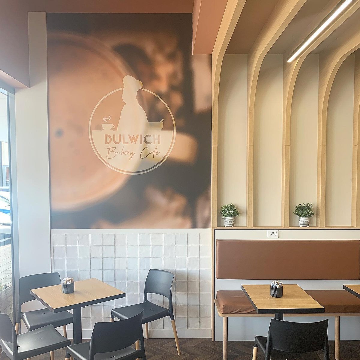 Modern cafe interior with Dulwich Beauty Cafe signage, dining tables, chairs, and geometric wood-paneled wall accents