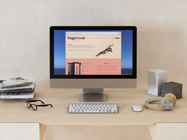 Desktop workspace with iMac displaying a website, keyboard, mouse, glasses, and office supplies on a wooden desk
