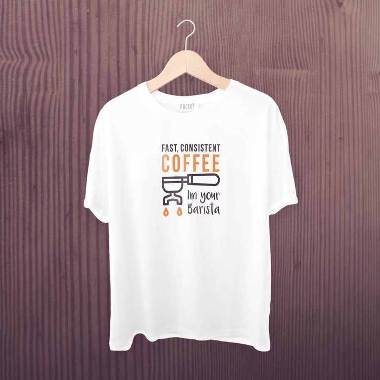 White t-shirt on wooden hanger with coffee-themed graphic text and espresso machine illustration