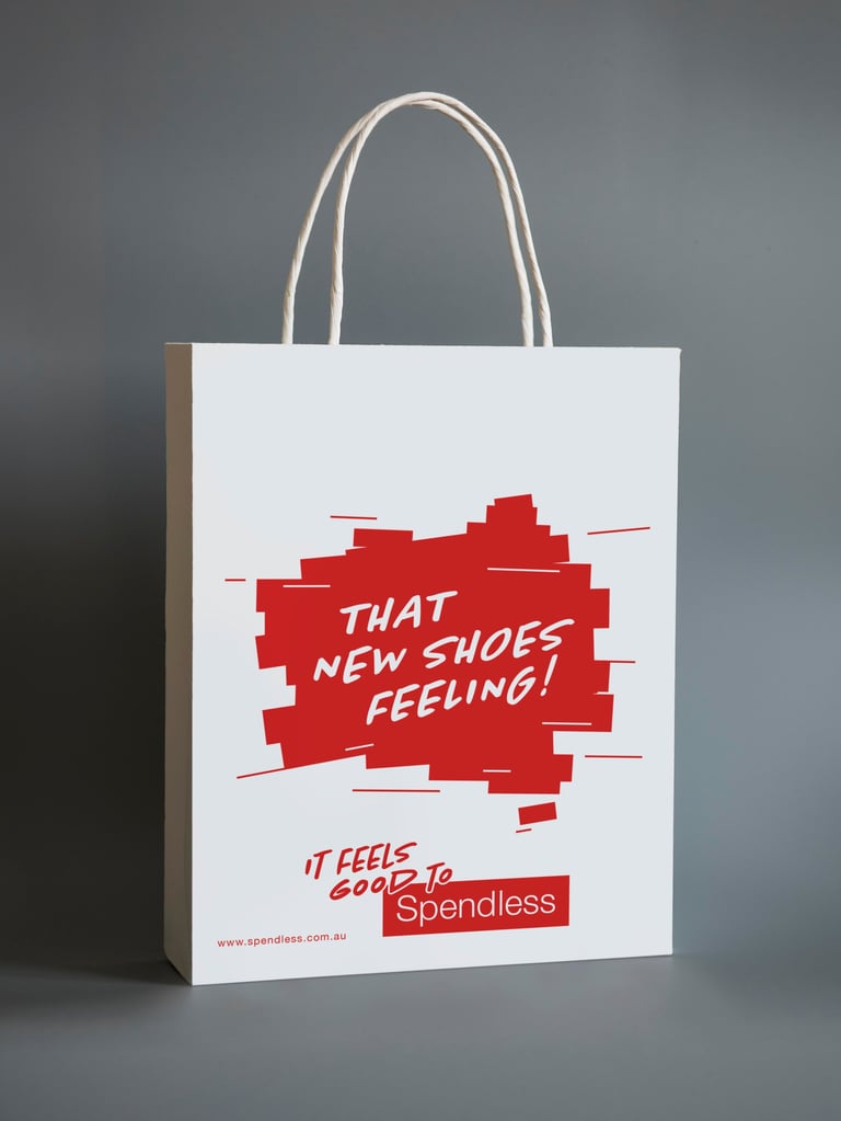 White shopping bag with gray handles displaying red graphic text reading That New Shoes Feeling and Spendless branding