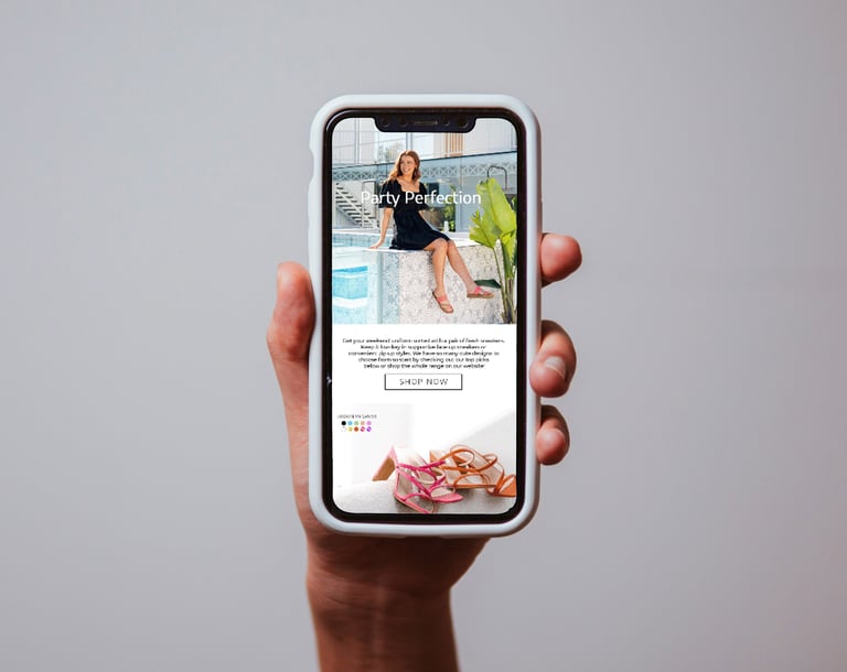 Hand holding smartphone displaying a fashion website with woman in black outfit and product images