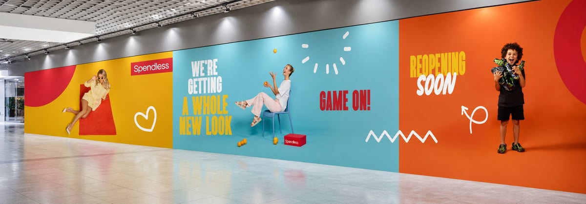 Colorful indoor wall mural with text reading Game On, Coming Soon, and Were Getting Started, featuring illustrated people and geometric shapes in red, yellow, and blue