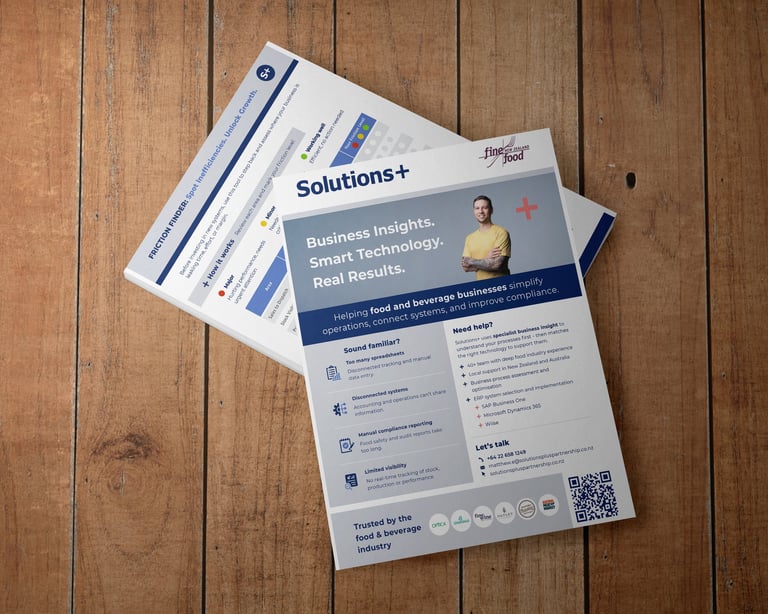 Business marketing brochures stacked on wooden surface, featuring Solutions+ materials with blue and white design