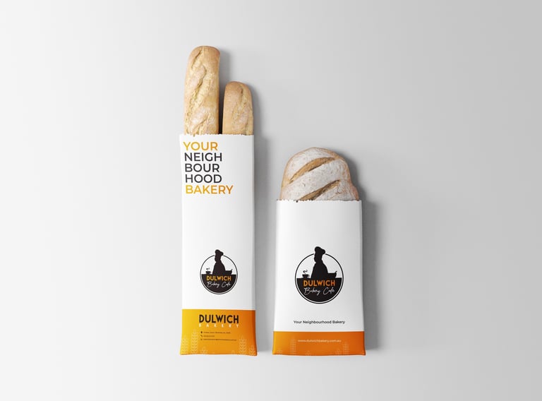 Two white paper bakery bags with baguettes and round bread, featuring Neighbourhood Bakery branding and yellow and orange accent bands