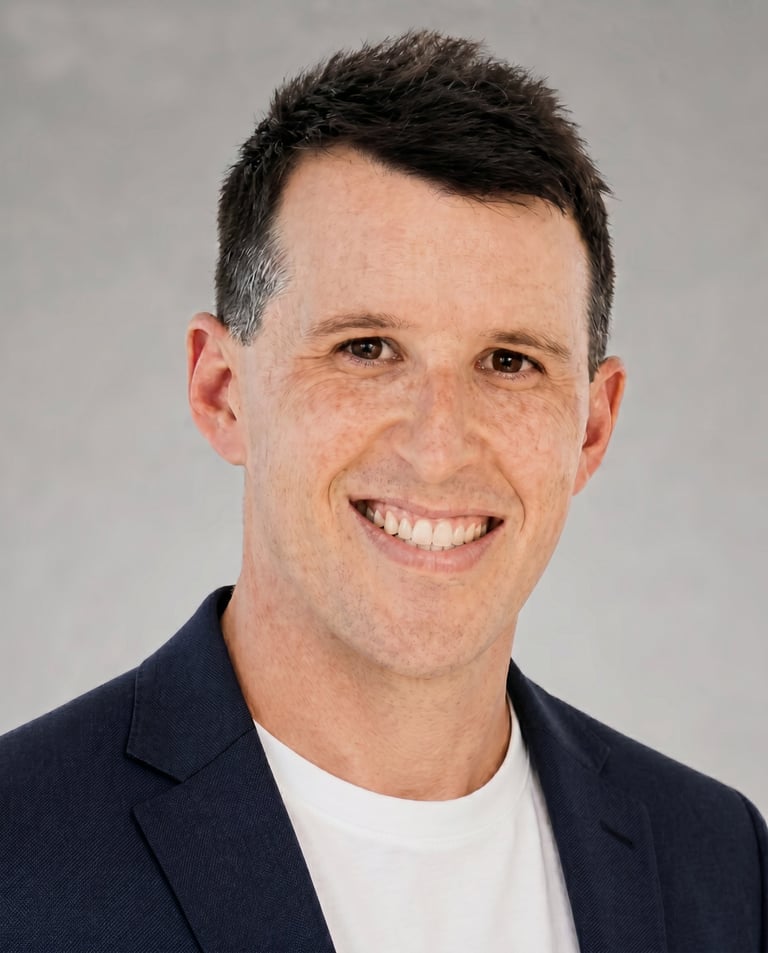 Professional headshot of a smiling man with dark hair wearing a navy blazer and white shirt against a gray background