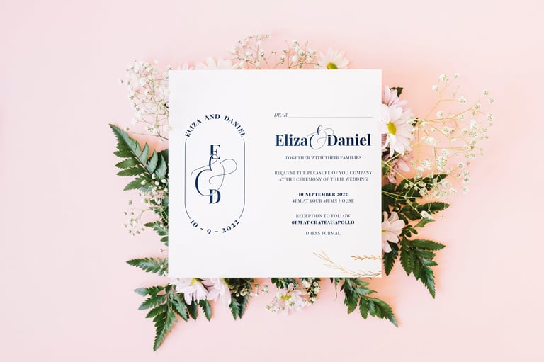 Wedding invitation card with initials E and D surrounded by fresh flowers and green leaves on pink background